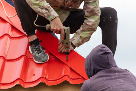 Workers install red metal tiles on the roof of the house.のeditorial素材