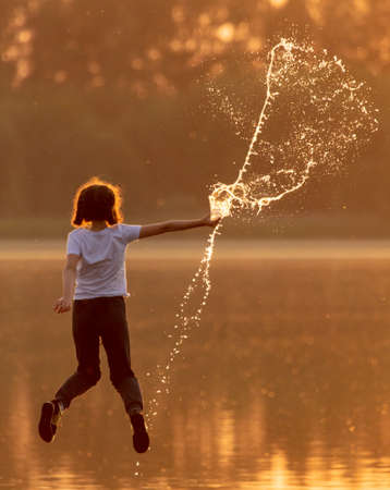 Children play with splashes of water at sunset in summer.のeditorial素材