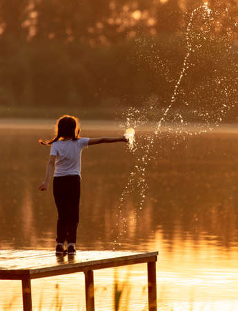 Children play with splashes of water at sunset in summer.の写真素材