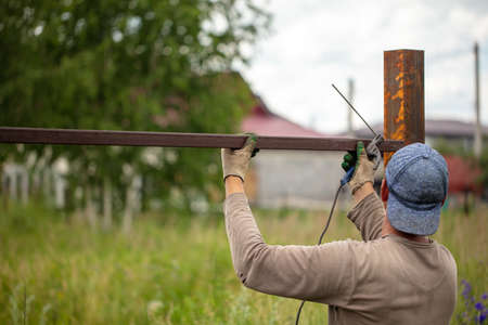 Worker installs a metal fence in the summer. Weldingの写真素材
