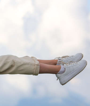 The legs of a girl in sneakers are flying in the clouds.の写真素材