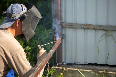 Worker installs a metal fence in the summer. Welding