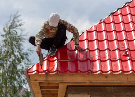 Workers install red metal tiles on the roof of the house.の写真素材