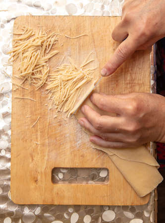A woman cuts noodles from dough with a knife.