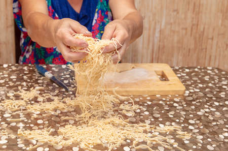 A woman sprinkles noodles cut from dough on the table.