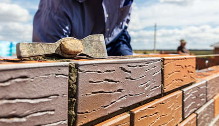 The worker lays bricks on the wall of the house. Construction
