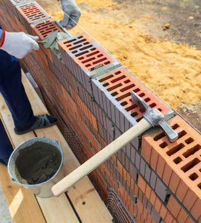 The worker lays bricks on the wall of the house. Construction