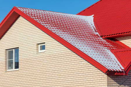 White snow lies on the red roof of the house. Winterの写真素材