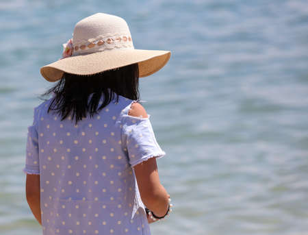 A girl in a hat walks on the beach by the sea.の写真素材