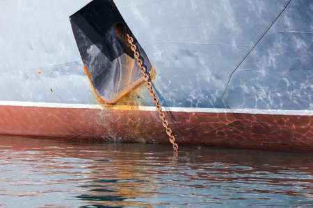 A rusty metal chain descends into the water from the ship. The ship is in port