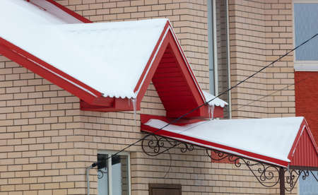 White snow lies on the red roof of the house. Winter