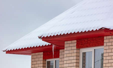 White snow lies on the red roof of the house. Winter