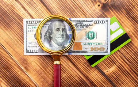 Close-up of one hundred dollars in a magnifying glass on the table.
