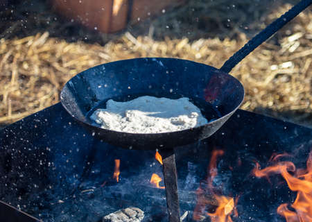 Pancake is fried in a pan over the fire.の写真素材