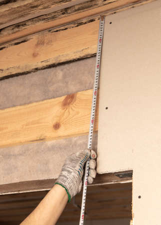 A worker measures drywall for a wall in a room. Repair.