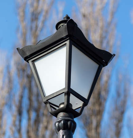 Lantern on a metal pole in the park against the blue sky.