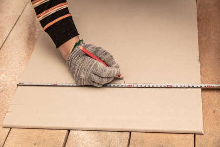 A worker measures drywall for a wall in a room. Repair.