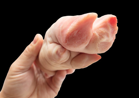 Pork hoof feet in hand isolated on black background.