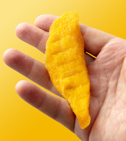 Dried mango in hand isolated on yellow background. Close-upの写真素材