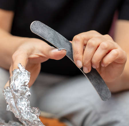 The girl removes the nail polish with a file and foil. Manicure close-upの写真素材