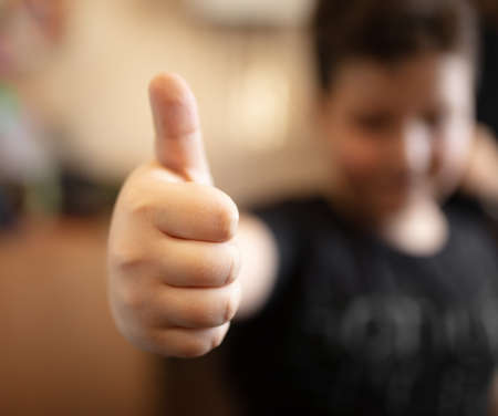 The boy shows a thumb up on his hand. Close-up
