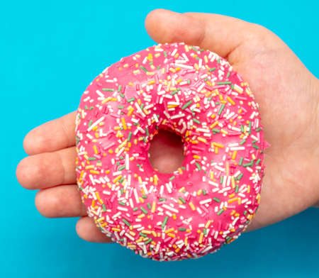 Red donut in hand on a blue background. Close-upの写真素材
