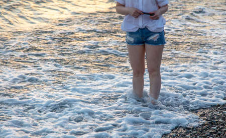 Girl in shorts in the sea water at sunset.の写真素材