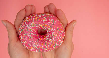 Red donut in hand on a pink background. Close-upの写真素材