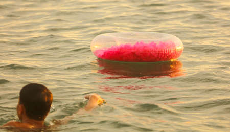 The boy swims with a rubber ring in the sea at sunset.の写真素材