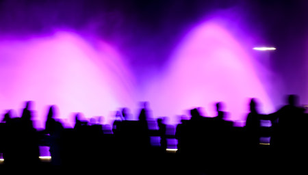 Silhouettes of people in motion near a colored fountain at night. Backgroundの写真素材