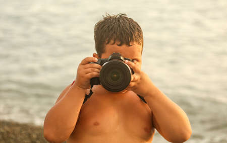 Boy with a camera in his hands at the sea at sunset.の写真素材