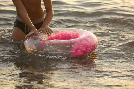 The boy swims with a rubber ring in the sea at sunset.の写真素材