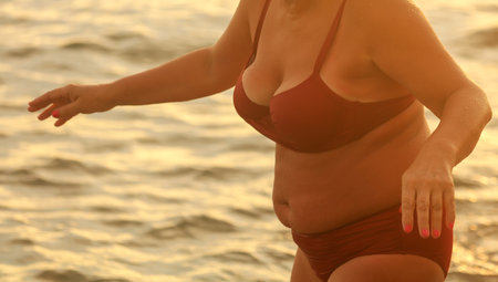 Fat woman in a swimsuit at sunset.の写真素材