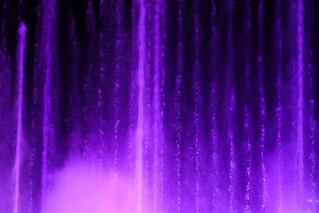 Splashing fountain in purple color at night as background.の写真素材