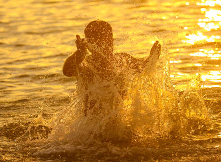 Boy swims in the sea with splashes at sunset.