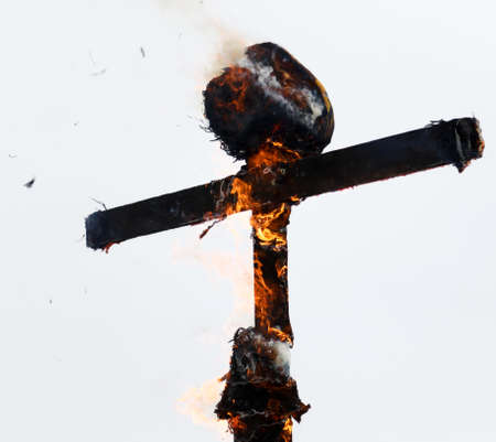 A wooden cross is burning with fire against a gray sky.の写真素材