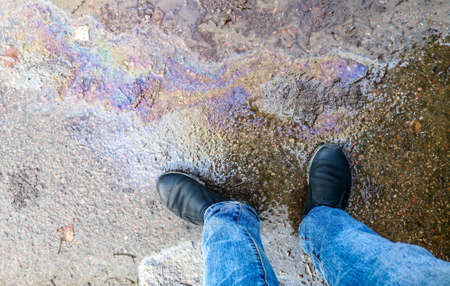 Gasoline in a puddle on the road. Mens feet in shoesの写真素材