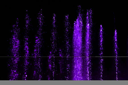 Splashing fountain in purple color at night as background.