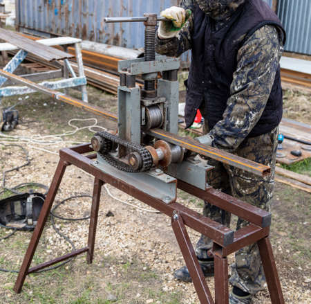 Workers bend metal in a pipe bender. Construction site technology