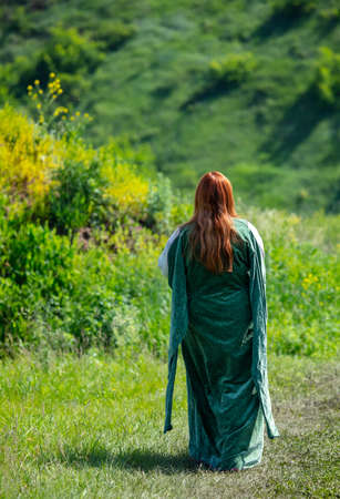 A woman in a long dress walks on the grass in the field.
