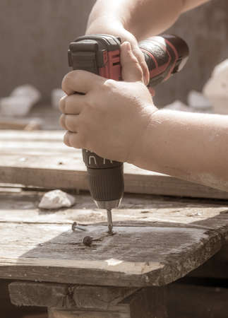 A boy twists a self-tapping screw into a wooden board.の写真素材