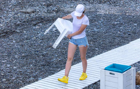 Girl with a chair on a pebble beach by the sea.の写真素材