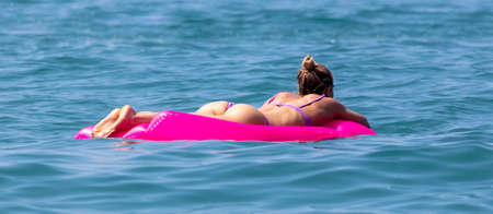The girl floats on a red inflatable mattress on the sea.