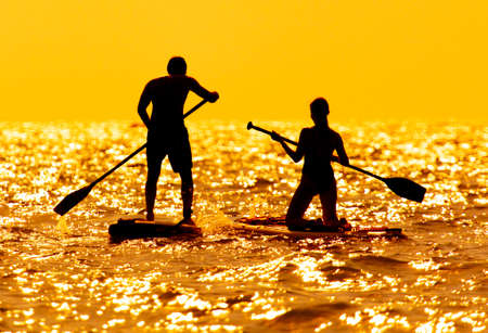 A man and a girl are sailing on a board in the sea. Sunsetの写真素材