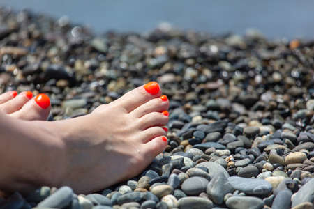 Red pedicure on a girl's leg on a pebble beach. Close-upの写真素材