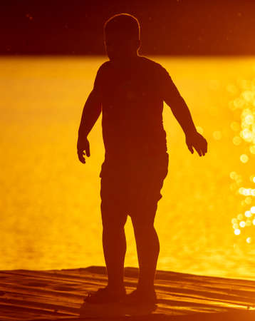 Silhouette of a boy on the lake. Sunset