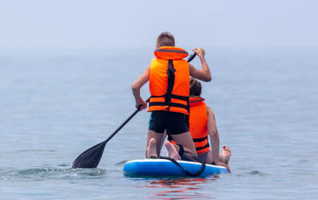 A man and a girl are sailing on a board in the sea.