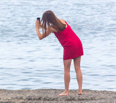 The girl takes pictures with her phone on the beach by the sea.の写真素材