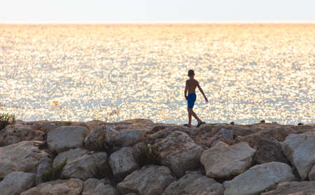Boy on the rocky land by the sea.の写真素材