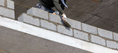 A worker lays bricks on a wall at a construction site.